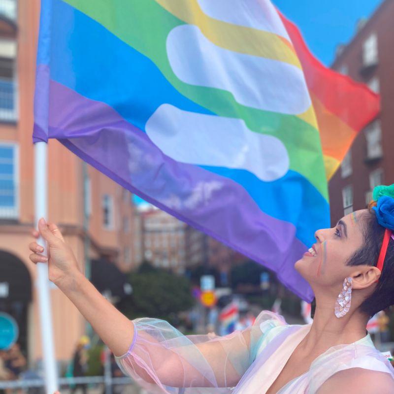 person wearing earrings and face paint waving an ericsson pride flag
