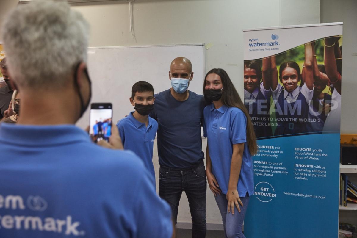 Pep Guardiola poses for a picture with two people wearing Xylem shirts