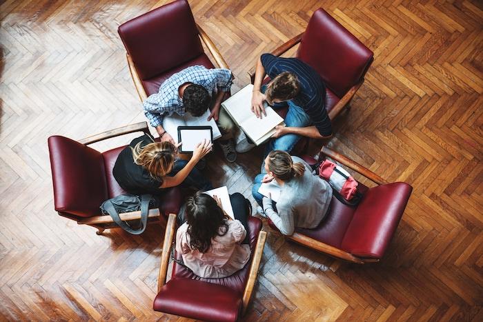 Overhead photo of five students sitting in a circle comparing notes.