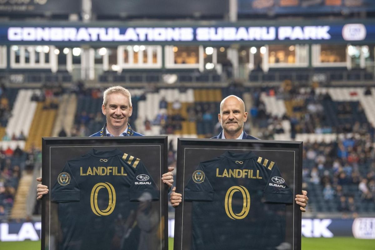 Two people holding up soccer jerseys with the words "Landfill 0"