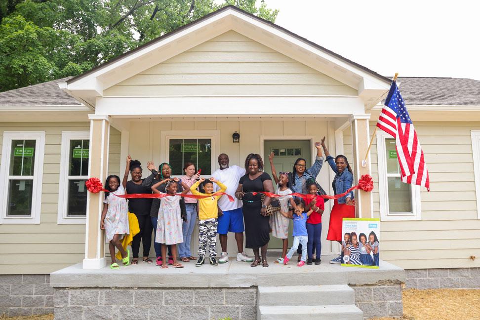 Latonya and her family cutting a red ribbon in front of her new home