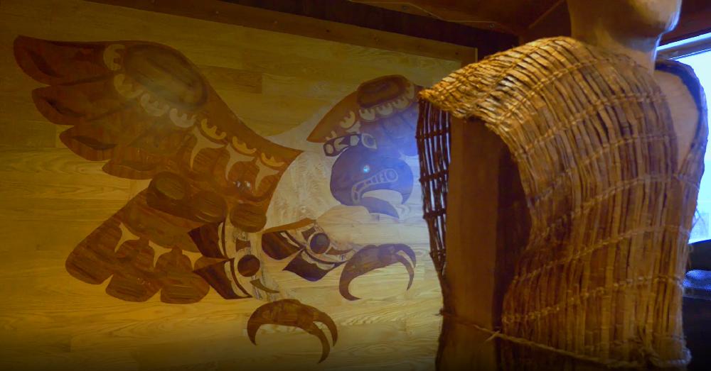 Bird of prey depicted in inlaid wood beside a basket woven out of cedar bark.