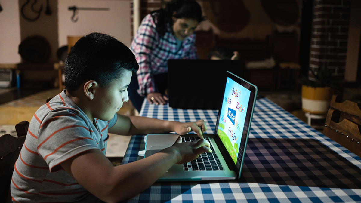 A child sitting at a desk working on a laptop, the glow from the screen lights up their face.