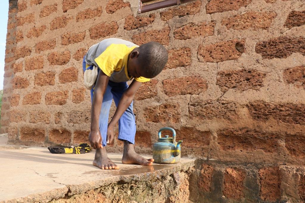 Konkourona child washes their feet with water from a small kettle