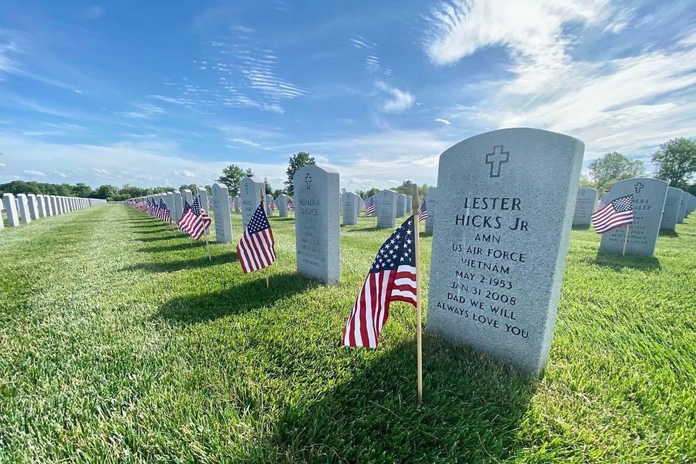 Close up of a headstone at a service member cemetery. American flags planted in front of each stone.